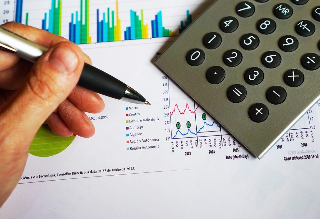 A person holding a pen over a financial chart with a calculator nearby